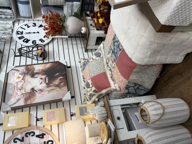 A styled bedroom vignette with a patchwork quilt, wall clocks, and framed art at Trendys Clothing