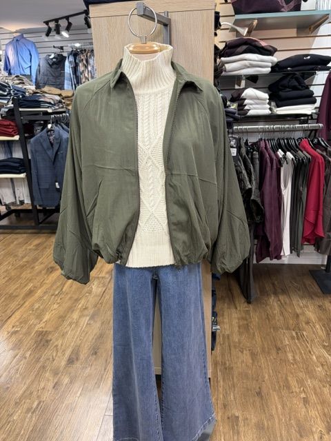 An olive bomber over a cream cable-knit with wide-leg jeans