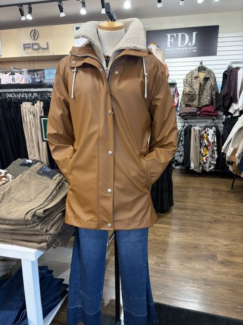 A camel rain jacket with a sherpa-lined hood styled with flared jeans, in front of the FDJ display at Trendys